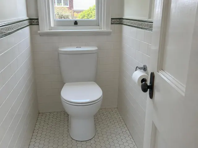 Clean white toilet in a tiled bathroom with a window and patterned floor in Dulwich Hill