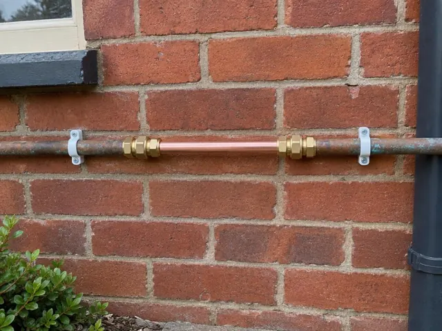 Repaired copper water pipe section on a red brick exterior wall in Marrickville